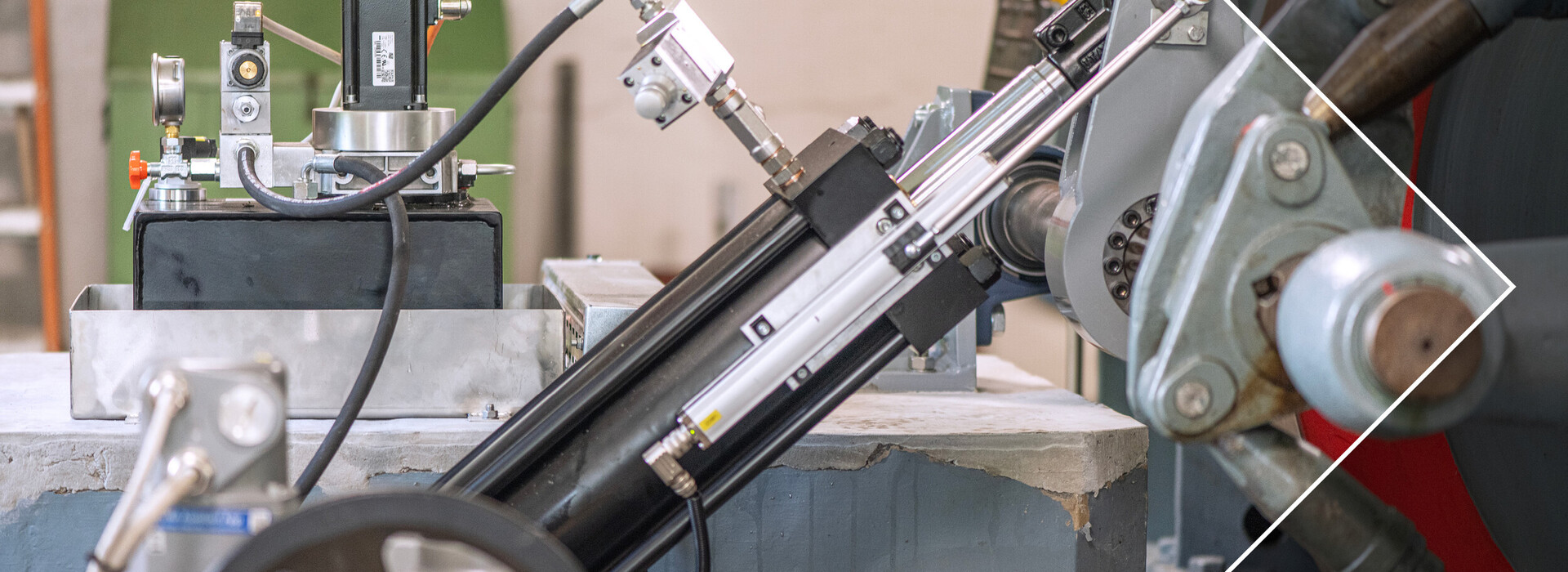 Nahaufnahme einer technischen Vorrichtung mit Zylindern, Schläuchen und Metallteilen in einer Werkstattumgebung.