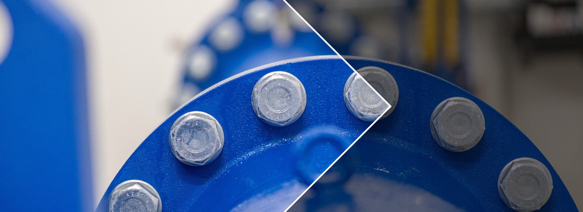 Close-up of a blue metal pipe with multiple bolts on the joint, left half of the image blurred, right half sharp.
