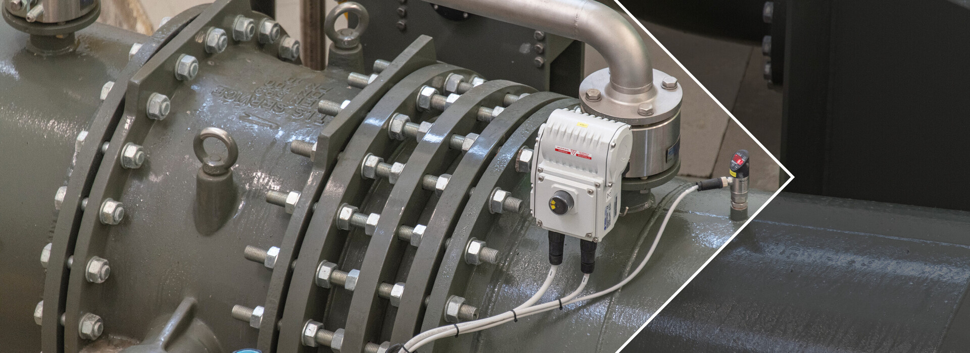 Close-up of a gray industrial valve with metal pipe and white measuring device.