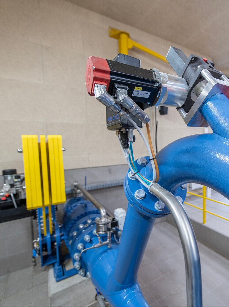 Close-up of a blue pipe system with an attached measuring device in a technical room.