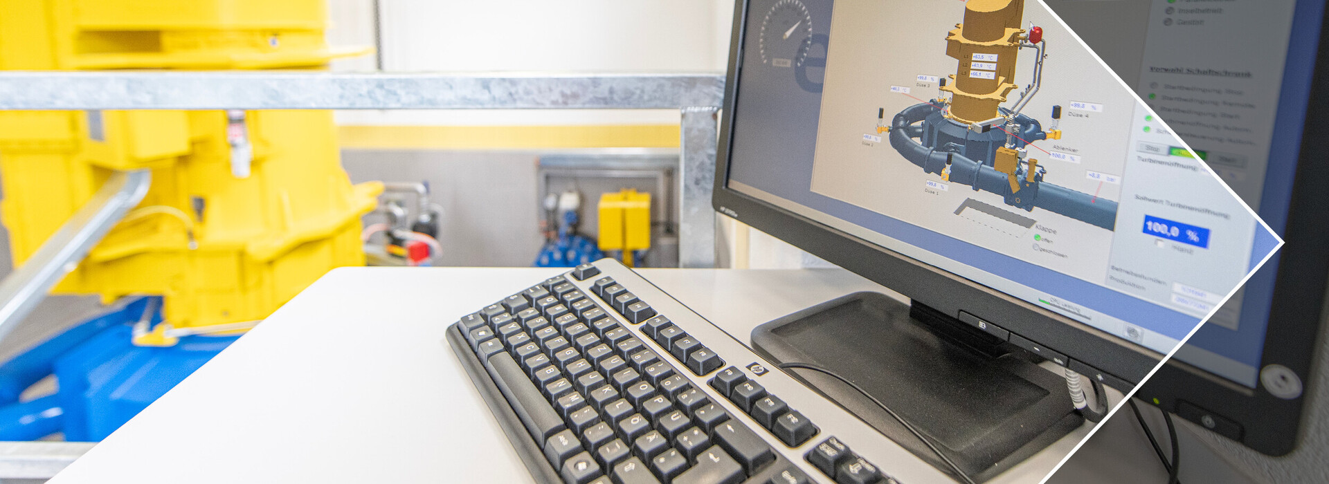 Computertastatur und Monitor mit technischer Grafik in einem hellen Raum mit gelben Wasserkraftwerk im Hintergrund.