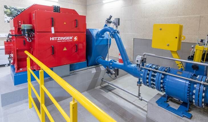 Rotes Wasserkraftwerk mit blauem Rohrleitungssystem in einem technischen Raum mit gelbem Geländer.