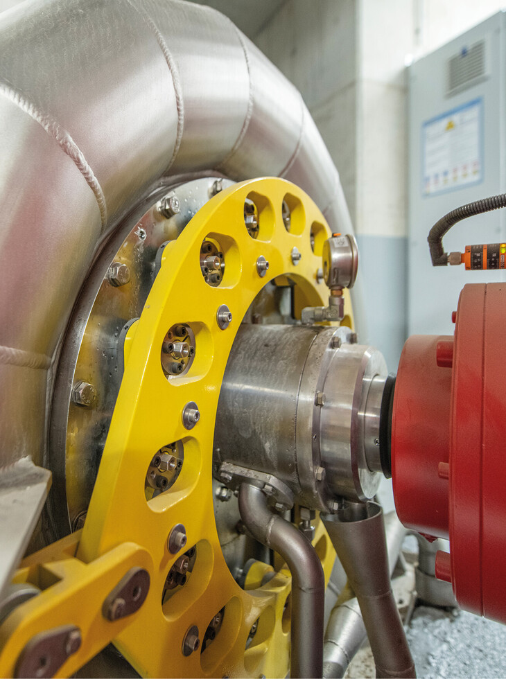 Nahaufnahme eines Turbine mit gebogenem Metallrohr, gelbem Halter und rotem Bauteil in einer Industrieumgebung