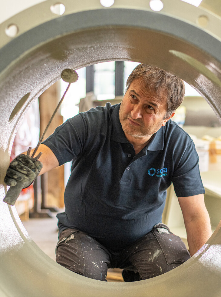 Craftsman in dark blue polo shirt with logo sora working with brush on large metal ring.