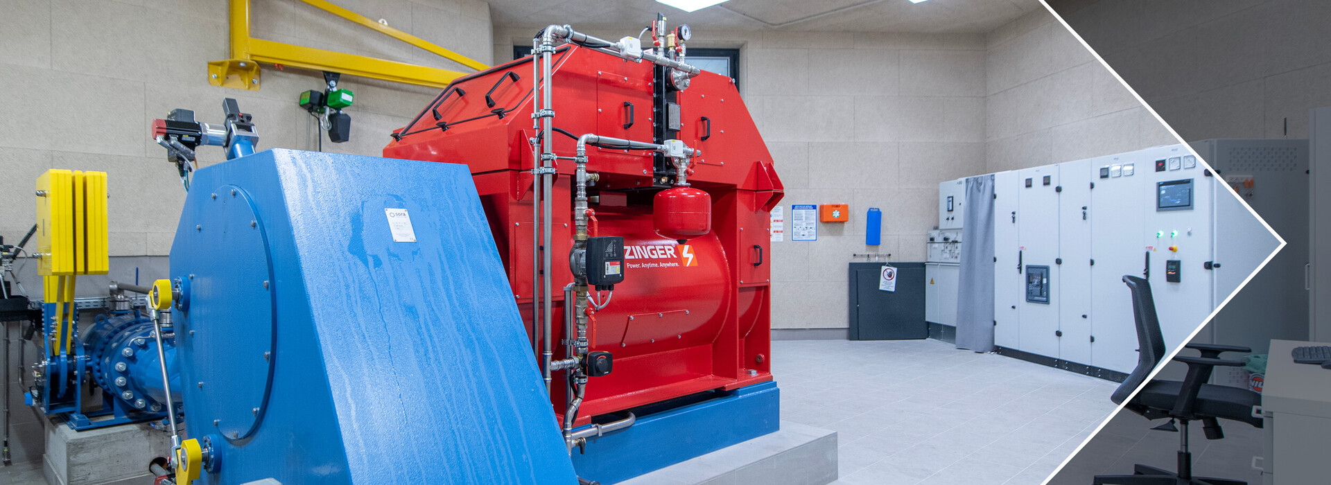 Technical room with red hydroelectric power plant, blue drive and switch boxes on the wall.
