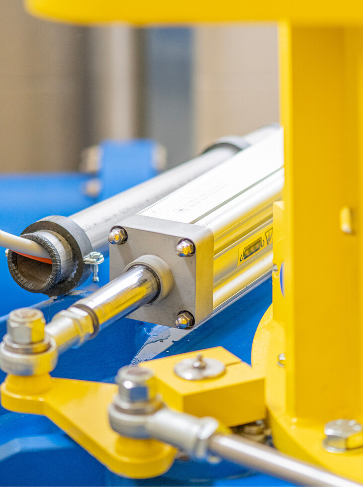 Close-up of a pneumatic cylinder with yellow and blue machine parts.