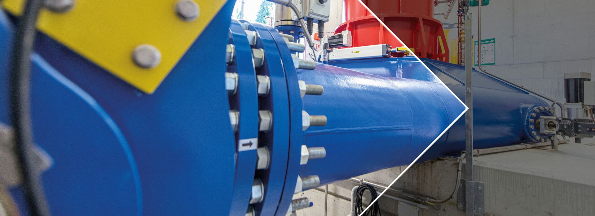 Primo piano di una sezione di tubo blu con una staffa gialla e diverse viti in un impianto industriale con una centrale idroelettrica.