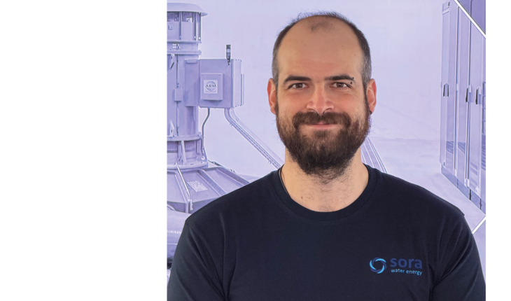 Oberkörper eines Mannes mit Bart, der ein schwarzes T-Shirt mit dem Logo und Schriftzug 