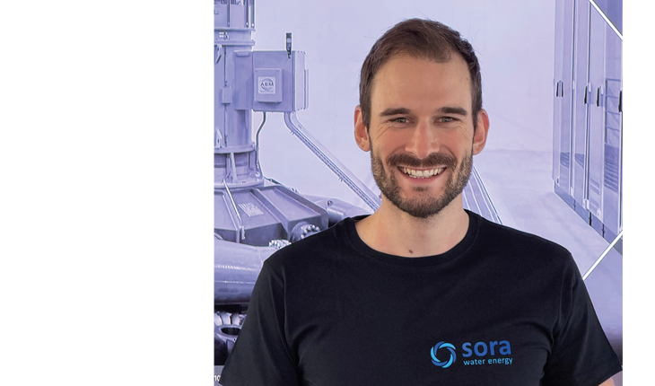 Il torso di un uomo con la barba, che indossa una maglietta nera con il logo e la scritta 