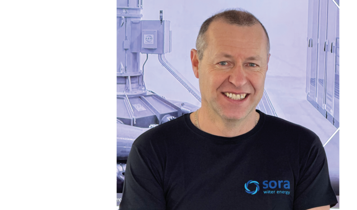 Oberkörper eines Mannes mit kurzem Haar, der ein schwarzes T-Shirt mit dem Logo und Schriftzug 